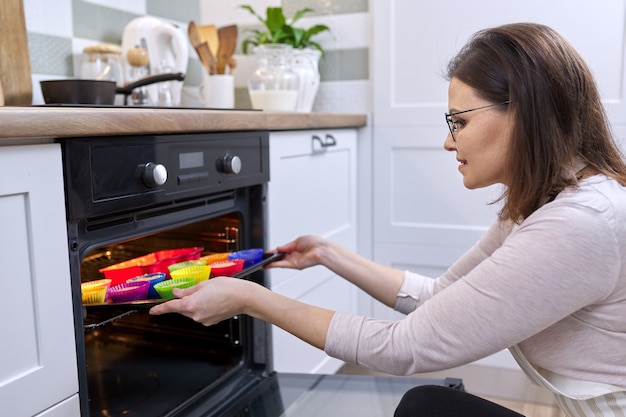 Femme en tablier préparant des cupcakes à la maison. Femme au foyer sortant cuire au four avec des muffins cuits au four, nourriture saine faite maison, passe-temps