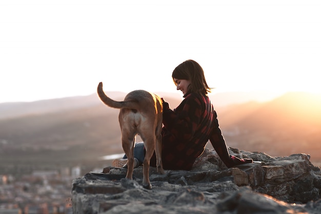 Photo fille avec son chien dans un rocher avec coucher de soleil