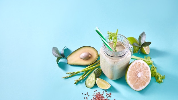 Photo fruits et légumes verts fraîchement cueillis, graines de lin pour préparer un smoothie végétarien sain dans un bocal en verre sur bleu. mise à plat.