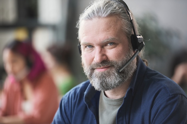 Gros plan d'un travailleur d'appel barbu mature dans un casque regardant la caméra