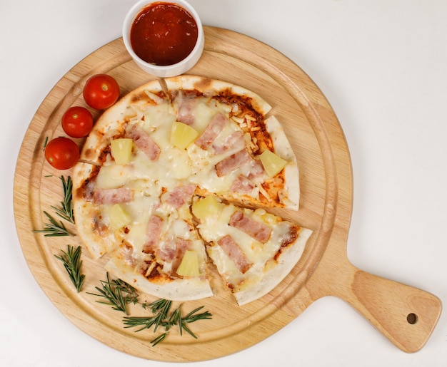 Gros plan vue de dessus prise de vue en studio d'un four chaud rond cuit au four savoureux délicieux jambon italien fait maison ananas original hawaïen pizza à la croûte de pain moelleux sur une plaque en bois avec des tomates et du ketchup sur la table