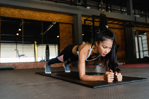 Heureuse jeune femme asiatique faisant de la planche à brûler les graisses en classe de fitness.