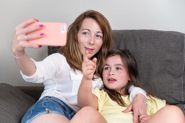 Heureuse mère avec sa fille passe un appel vidéo au père ou à des proches dans un canapé Concept de technologie nouvelle génération connexion familiale parentalité