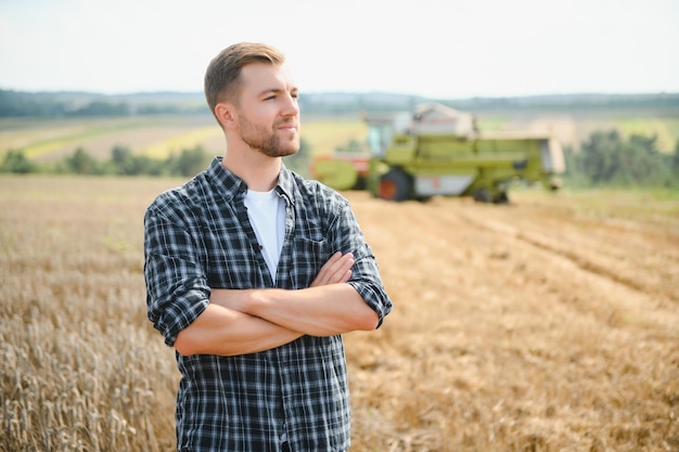 Heureux agriculteur fièrement debout dans un champ Conducteur de moissonneuse-batteuse allant récolter une riche récolte de blé Agronome portant une chemise en flanelle regardant la caméra sur une terre agricole