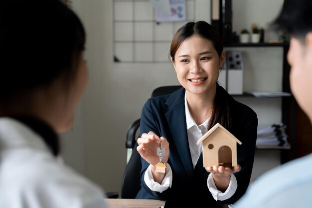 Photo heureux couple familial faisant l'achat de leur première maison en prenant la clé de l'agent immobilier féminin vue de derrière les clients concept d'agence immobilière