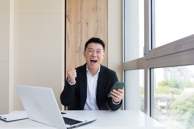 Photo heureux jeune homme d'affaires asiatique au bureau regardant la caméra avec les émotions du gagnant