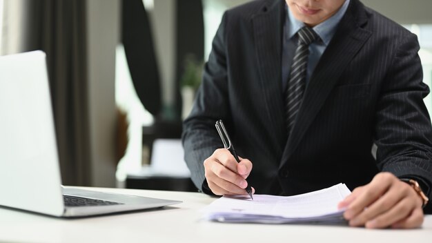 Photo un homme d'affaires confiant en costume noir écrit des notes ou un rapport financier dans un bureau moderne.