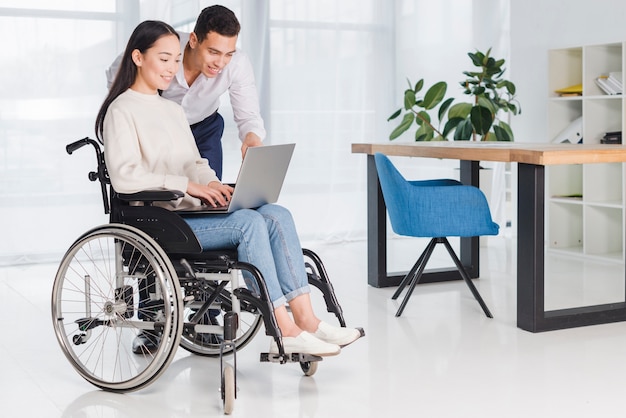 Homme d&#39;affaires souriant montrant quelque chose à sa jeune femme handicapée sur ordinateur portable au bureau