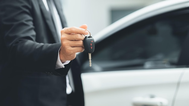 Un homme en costume se tient tenant les clés de la voiture à côté d'une voiture blanche qui obtient une nouvelle voiture avec un concessionnaire automobile