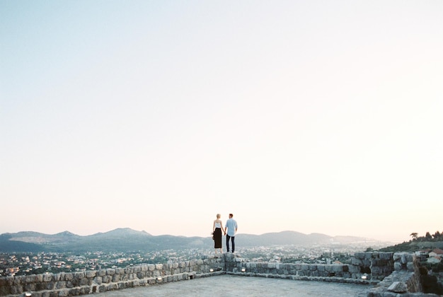 L'homme et la femme se tiennent sur un mur de pierre et regardent le panorama des montagnes Vue arrière