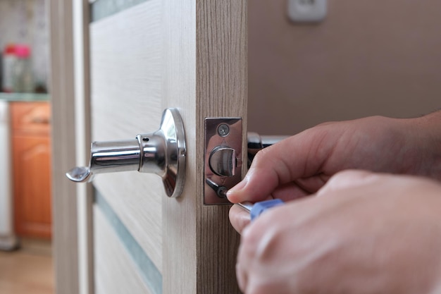 Un homme répare la serrure de la porte intérieure avec un tournevis