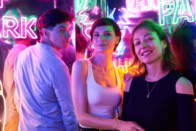 Image de deux belles femmes et d'un homme dans un parc d'attractions dans une pièce éclairée au néon Concept de divertissement