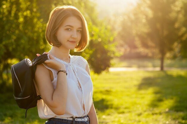 Jeune adolescente aux cheveux courts avec sac à dos dans le parc au coucher du soleil