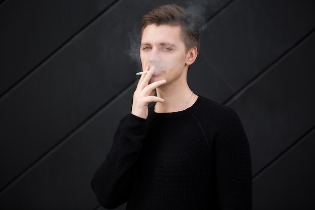 Photo jeune beau mec fumer une cigarette sur fond noir