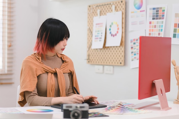 Photo une jeune designer indépendante créative et élégante utilise une tablette et un stylet alors qu'elle est assise à son bureau au bureau.