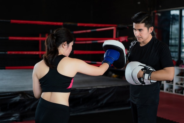 Jeune femme asiatique boxeur frappe avec un coup de poing droit à un entraîneur professionnel dans un stade de boxe