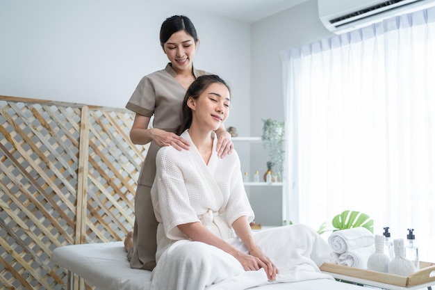 Photo une jeune femme asiatique heureuse se sent relaxée pendant le massage des épaules et du dos une belle fille attrayante assise sur la table de massage recevant un service de physiothérapie d'une masseuse pour les soins du corps dans un salon de beauté spa