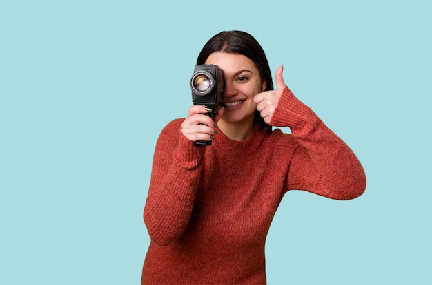 Une jeune femme filme joyeusement avec une caméra vidéo antique sur un fond isolé