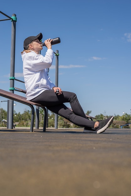 Jeune femme sportive dans des gants de sport buvant de l'eau sur un terrain de sport