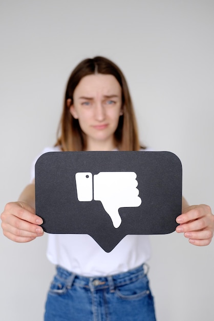 Photo une jeune femme triste tenant l'icône du bouton dislike des médias sociaux