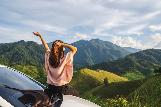 Photo jeune femme voyageur assis dans une voiture en regardant une belle vue sur la montagne pendant le voyage au volant d'un voyage sur la route en vacances