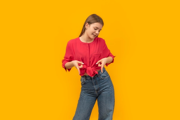 Jeune fille en vêtements de jeunesse sur fond orange pointe les doigts vers le bas Portrait d'adolescent Espace de copie