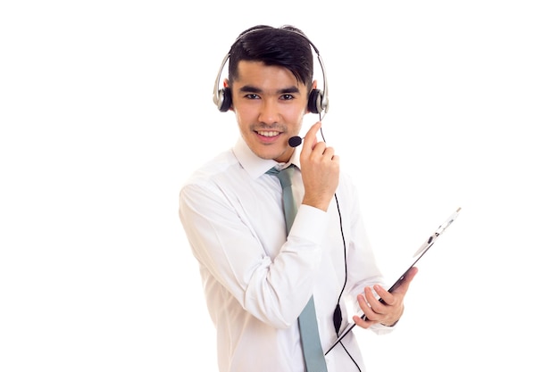 Jeune homme heureux aux cheveux noirs en chemise blanche avec cravate bleue et casque tenant un dossier sur fond blanc en studio