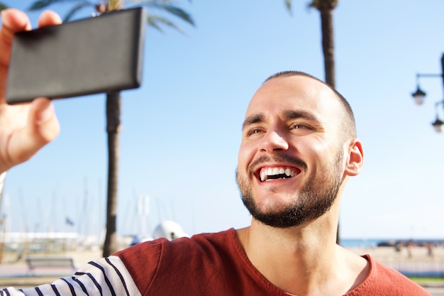 Photo jeune homme en riant en prenant un selfie avec un téléphone mobile