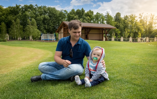 Jeune père souriant avec son bébé se reposant sur l'herbe au parc aux beaux jours