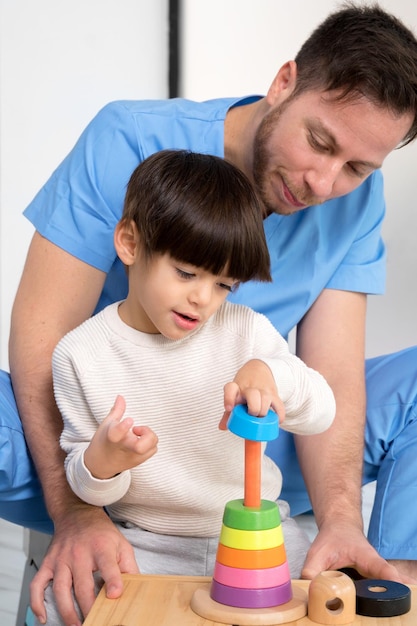 Jeune thérapeute aidant un petit garçon mignon atteint de paralysie cérébrale en jouant avec un jouet en développement à la réhabi...