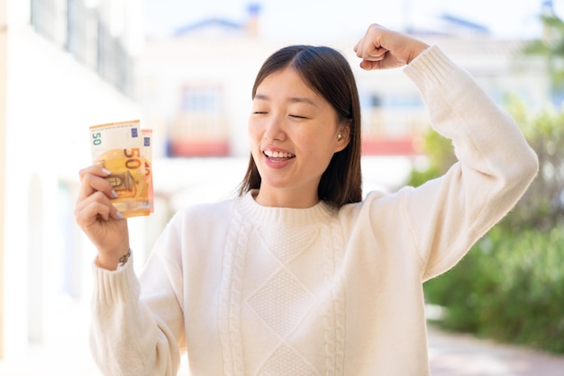 Photo jolie femme chinoise à l'extérieur prenant beaucoup d'argent et célébrant une victoire