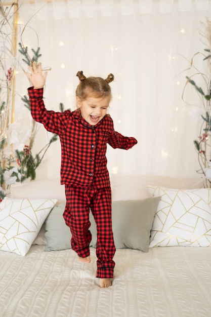 Photo une jolie petite fille en pyjama rouge de noël sautant sur le lit s'amusant