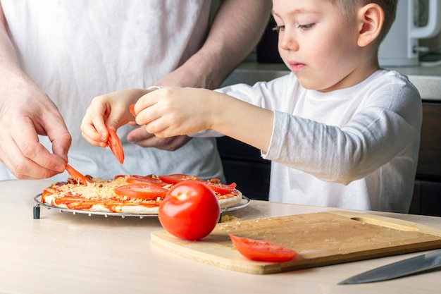 Kid aide son père à cuisiner des pizzas maison. Passe-temps en famille pendant la quarantaine. Processus de cuisson de pizza par enfant. Restez à la maison, la distance sociale et l'auto-isolement.