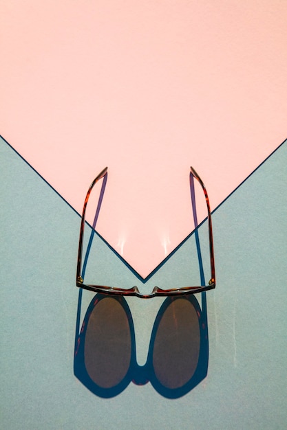 Lunettes de soleil d'été à la mode avec ombre portée sur fond rose et bleu