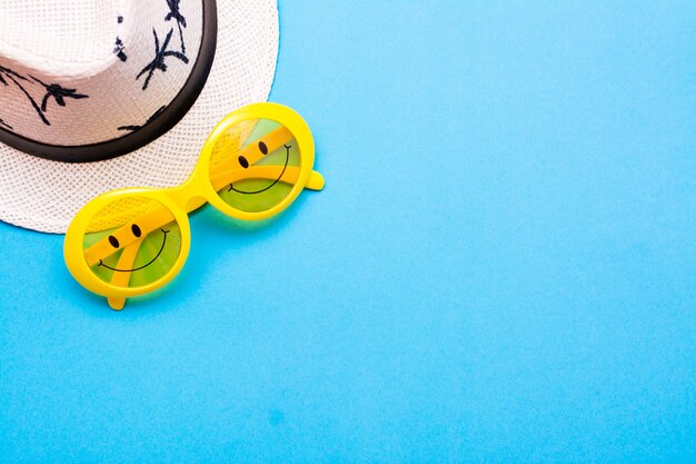 Photo lunettes de soleil en plastique jaune avec des yeux peints et un sourire sur les lunettes et un chapeau sur un fond bleu