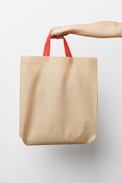Main féminine tenant un sac à provisions écologique ou réutilisable sur fond blanc