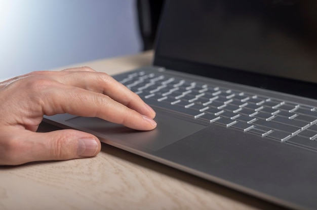 Main sur le pavé tactile de l'ordinateur portable tapotant et faisant défiler avec les doigts se bouchent