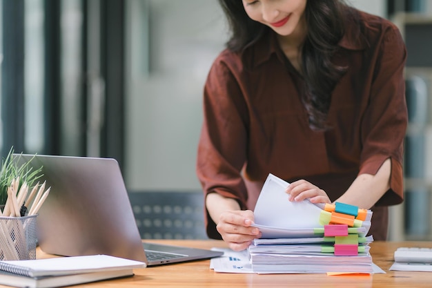 Photo les mains de la femme d'affaires sont occupées à travailler au milieu de piles de fichiers de papier à la recherche et à la vérification de documents inachevés parmi les dossiers et les papiers sur son bureau encombré