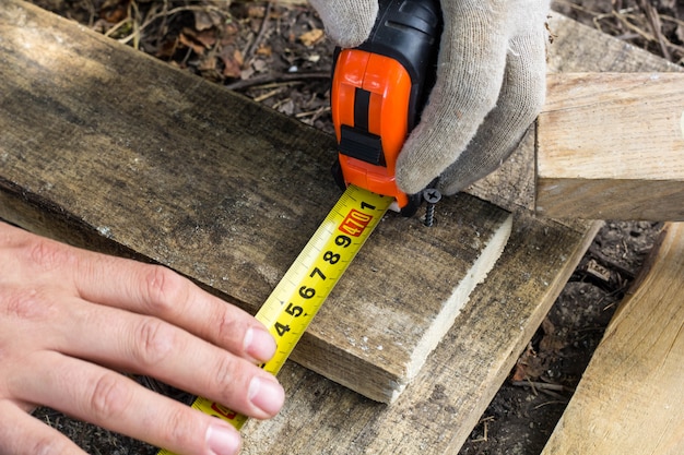 Photo mains d'hommes mesurant une planche de bois avec une roulette sur chantier