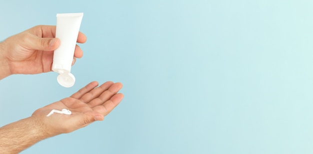 Mains mâles appliquent une crème hydratante cosmétique de soins de la peau ou une pommade sur fond bleu