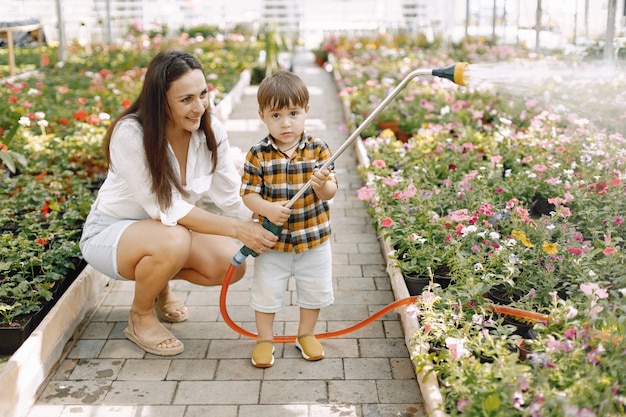 Maman et son fils avec un pulvérisateur d'eau dans la serre. Petit garçon enfant arrosant des fleurs dans une serre