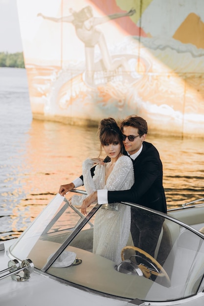 Le marié en costume noir et lunettes de soleil embrasse la mariée en robe de mariée sur un yacht par une journée ensoleillée