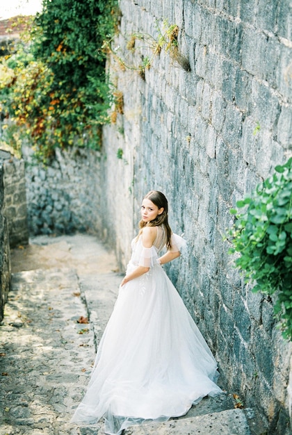 La mariée se tient sur les marches à côté du mur de pierre