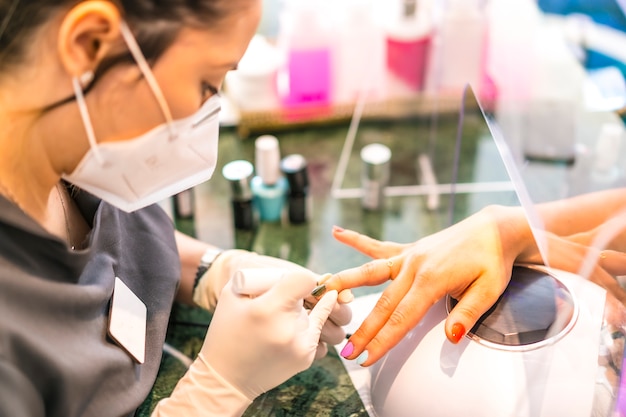 Avec masque facial peignant les ongles colorés du client. Réouverture après la pandémie de corod-19. Salon de manucure et pédicure. Coronavirus