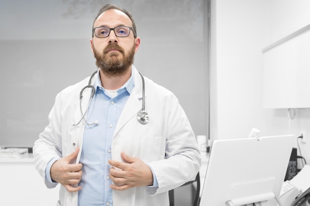 Médecin d'âge moyen portant une blouse médicale blanche à la clinique avec une expression sérieuse