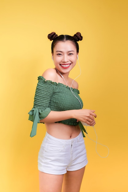 Photo mode femme asiatique souriante écoutant de la musique dans des écouteurs sur fond jaune