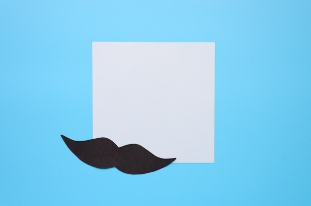 Photo moustache en papier noir et papier à lettres autocollant sur fond bleu. concept de sensibilisation à la santé masculine et au cancer de la prostate. movember. espace pour le texte