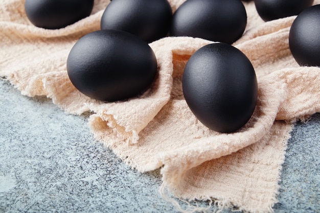 Oeufs de Pâques noirs sur une serviette en lin sur une table de texture bleue. Concept de célébration de Pâques.