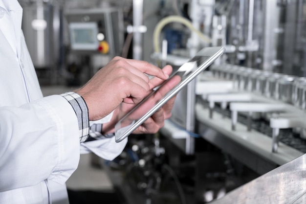 Ouvrier d'usine inspectant la chaîne de production d'une usine de boissons avec une tablette informatique