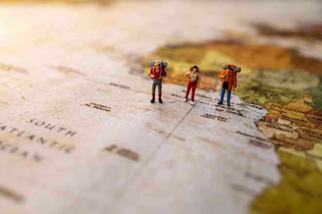 Photo personnes miniatures: voyager avec un sac à dos debout sur la carte du monde vintage, le concept de voyage et d'été.